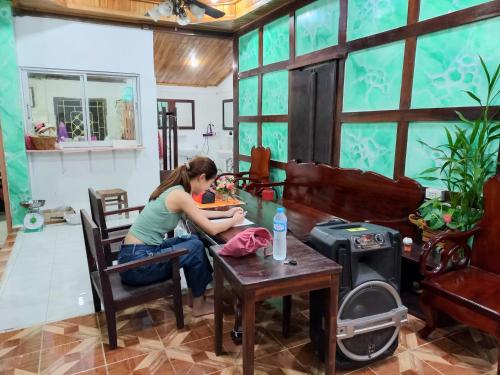 a woman sitting at a table in a room at Watthat & Maladreds GUESTHOUSE dorm 1 in Luang Prabang