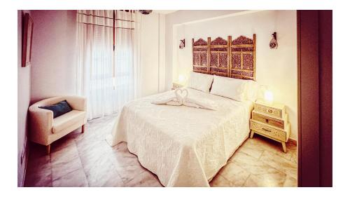 a bedroom with a white bed with a chair and a table at Al-Ladito in Córdoba