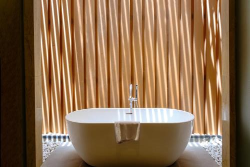 a white bath tub sitting in front of a window at Marianna Resort And Convention Tuktuk - Samosir, Marclan Collection in Tuk Tuk