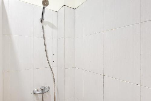 a shower with a hose in a white tiled bathroom at Papa Kana Farm Mitra RedDoorz At Pacet Mojokerto in Mojokerto