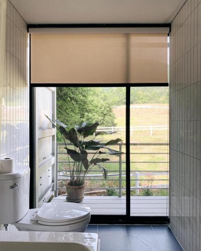 a bathroom with a toilet and a large window at Skugga Cabin in Mae On
