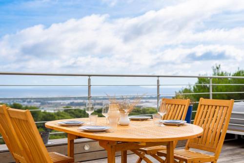 une table en bois avec des chaises et des verres à vin sur un balcon dans l'établissement Villa Mont des Oiseaux Hyères Piscine Vue Panoramique Mer Grande Terrasse, à Hyères