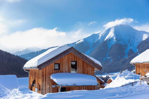 a building covered in snow with mountains in the background at Almdorf Hohentauern by ALPS RESORTS in Hohentauern