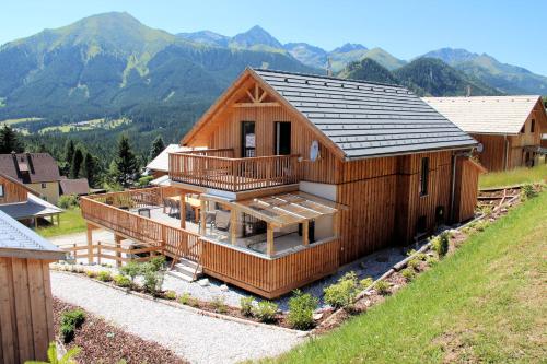 a wooden house with a deck and mountains in the background at Almdorf Hohentauern by ALPS RESORTS in Hohentauern