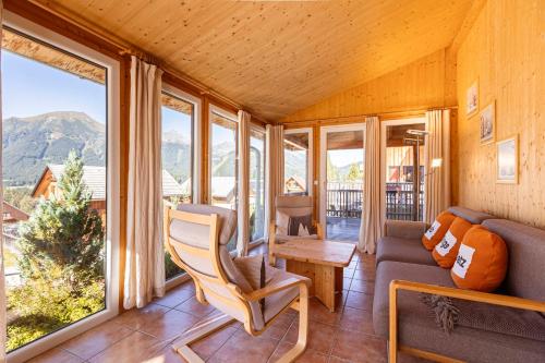 a living room with a couch and a table and windows at Almdorf Hohentauern by ALPS RESORTS in Hohentauern