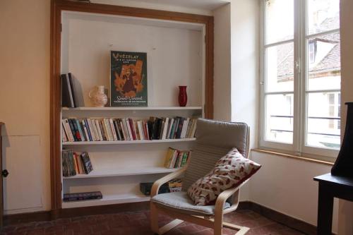 um quarto com uma cadeira e uma estante de livros com livros em Appartement -Le Clos- Cellier de l'abbaye em Vézelay