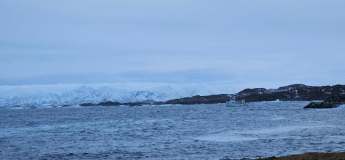 a boat in a body of water with snow covered mountains at Gamvik brakkebo as in Gamvik