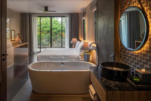 uma casa de banho com uma banheira, uma cama e um espelho. em Noku Phuket em Chalong