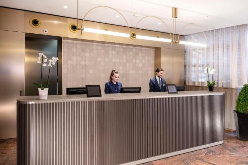 dos personas sentadas en una recepción en un vestíbulo en NH Geneva Airport Hotel en Ginebra