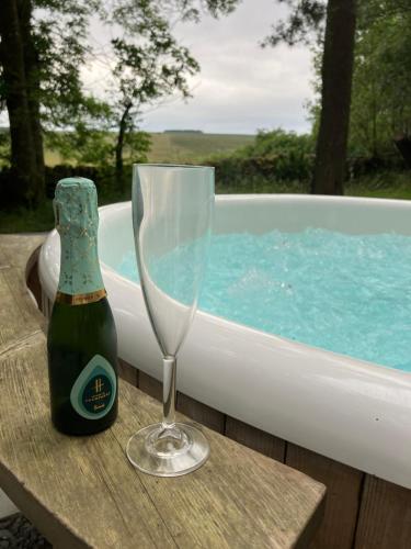 Una botella de champán y una copa en una mesa junto a una bañera. en Elishaw Farm Holiday Cottages, en Otterburn