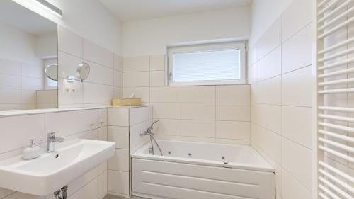 a white bathroom with a sink and a bath tub at DünenResort in Binz, strandnahe und moderne FeWos mit Balkon, teilweise mit Meerblick, in Binz