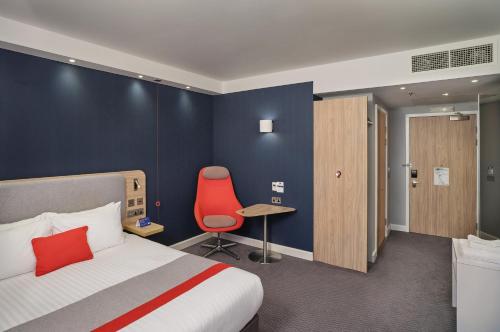 バーミンガムにあるHoliday Inn Express - Birmingham - City Centre, an IHG Hotelのベッドと赤い椅子が備わるホテルルームです。
