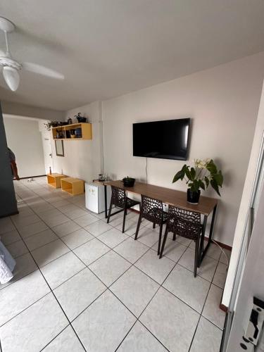 ein Wohnzimmer mit einem Tisch und einem TV an der Wand in der Unterkunft Quarto próximo à praia in Balneário Camboriú