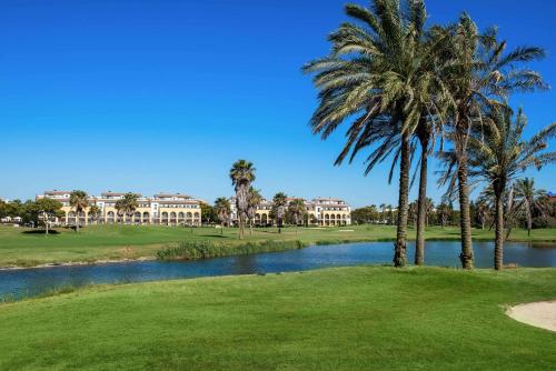 a golf course with palm trees and a pond at Barceló Costa Ballena Golf & Spa in Costa Ballena