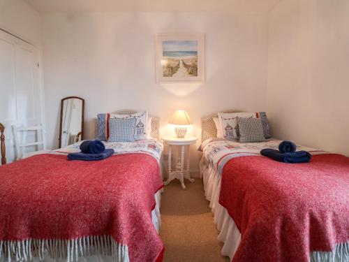 two beds in a room with red sheets at 3 Albion Cottages in Southwold