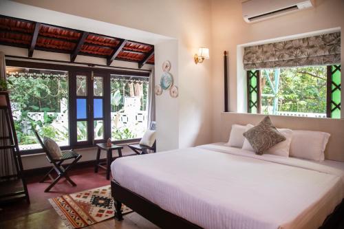 Lamrin Ucassaim Goa A 18th Century Portuguese Villa في Moira: غرفة نوم بسرير ابيض كبير ونوافذ