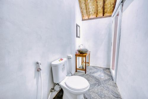 a white bathroom with a toilet and a window at Ananta Bungalow in Nusa Penida