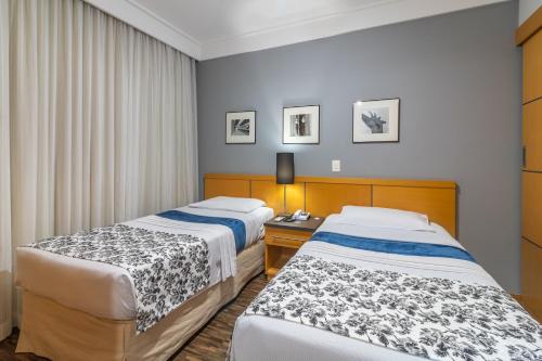 a hotel room with two beds and a desk at Green Place Ibirapuera in São Paulo