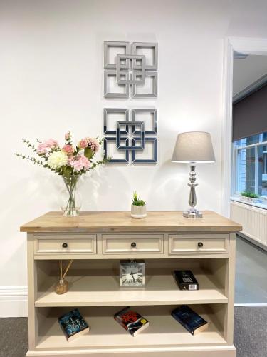 a wooden dresser with a lamp and flowers on it at Central penthouse by HNFC Stays in Newcastle upon Tyne