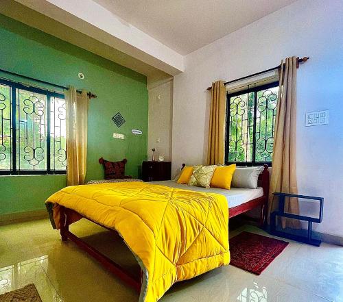 um quarto com uma cama amarela, paredes verdes e janelas. em Mitra Homes - Mandrem em Mandrem