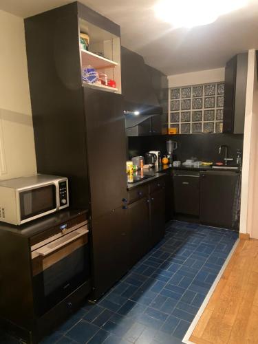 a kitchen with black cabinets and a microwave at Les Marais in Le Pré-Saint-Gervais