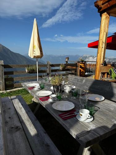 einem Holztisch mit Tellern, Tassen und einem Regenschirm in der Unterkunft Die Acherberg Alm in Oetz
