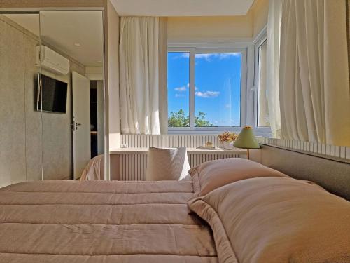 a bedroom with a large bed with a large window at Residencial Toscano 2 Suítes by Achei Gramado in Gramado