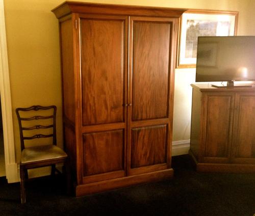 a wooden cabinet and a chair next to a television at The York Palace Accommodation in York