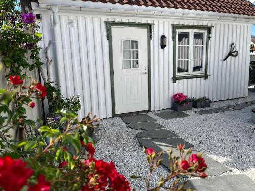 a white shed with a door and some flowers at Idyllisk lite anneks med enestående uteplass in Larvik