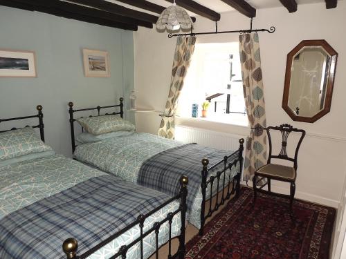 a bedroom with two beds and a mirror and a chair at 18th Century character cottage, Broughton-in-Furness in Broughton in Furness