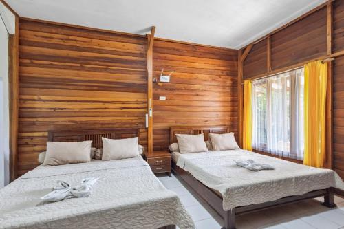 two beds in a room with wooden walls at Sawarna Little Hula Hula in Wangun