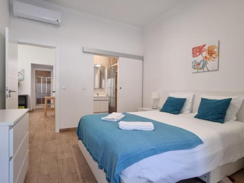 a white bedroom with a large bed with blue sheets at Oeiras 4 in Oeiras