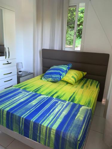 1 cama con edredón azul y verde y ventana en Maison dans les hauteurs en Le Gosier