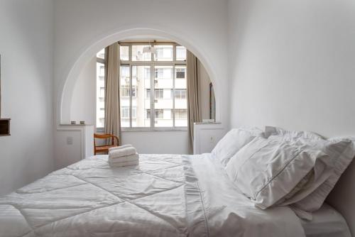 a white bedroom with a large bed with an arched window at Apartamento aconchegante em Copacabana - Rio de Janeiro in Rio de Janeiro