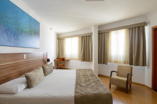 a hotel room with a bed and a chair at Faro Hotel São José dos Campos in São José dos Campos