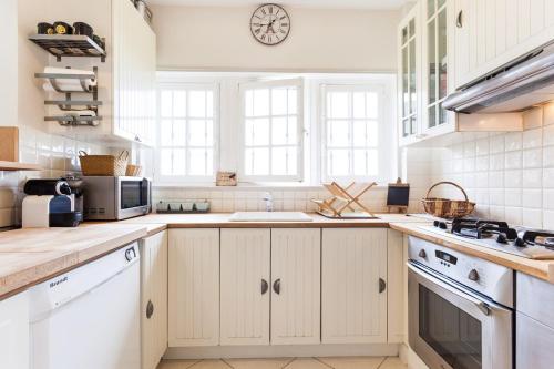 une cuisine avec des placards blancs et une horloge murale dans l'établissement Face plage, vue mer, jardin - Deauville, à Benerville-sur-Mer