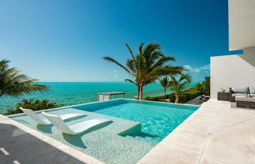 a swimming pool with two chairs and the ocean at Ocean Dream 5 BR Villa Aqua in Long Bay Hills
