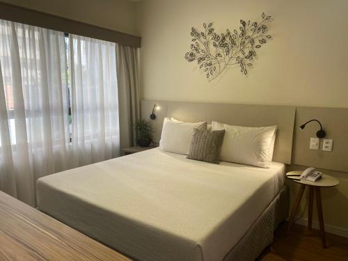 a bedroom with a large white bed with a window at Flat Jardins, entre Av Paulista e Parque do Ibiraquera in Sao Paulo