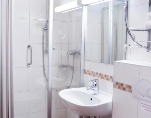 ein weißes Bad mit einem Waschbecken und einer Dusche in der Unterkunft Chalet Swiss - Appartementhotel in Bad Füssing
