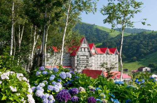 a building with a red roof with flowers in the foreground at Hotel Green Plaza Hakuba in Otari