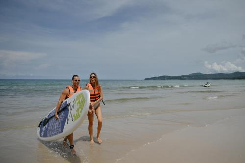 a man and woman walking on the beach with a surfboard at Arinara Beach Resort Phuket - SHA Extra Plus in Bang Tao Beach