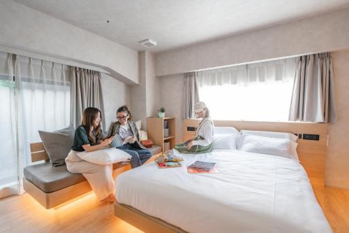 three women sitting on a bed in a hotel room at 脈 -MYAKU PRIVATE SAUNA- in Fukuoka
