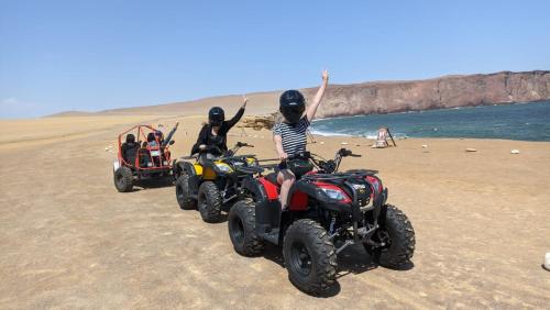three people riding atvs on a beach with their hands in the air at El Capricho Paracas in Paracas