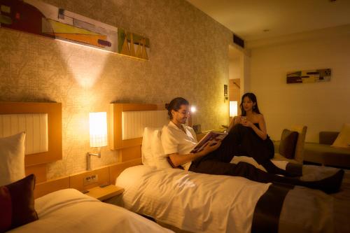 a man and woman sitting on a bed in a hotel room at Hotel Resol Trinity Kanazawa in Kanazawa