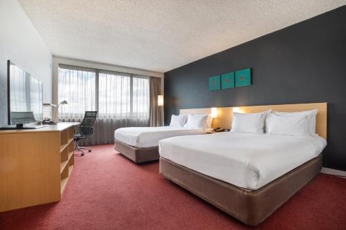 Holiday Inn Melbourne Airport, an IHG Hotel في ملبورن: غرفه فندقيه سريرين وتلفزيون