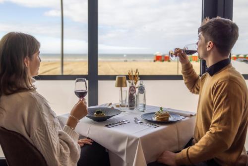 Ein Mann und eine Frau sitzen am Tisch und trinken Wein. in der Unterkunft Hotel Villa Select in De Panne