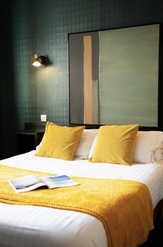 a large bed with yellow pillows and a book on it at Hôtel des Pins in Jullouville-les-Pins