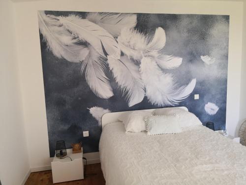 1 dormitorio con 1 cama con una pintura de plumas blancas en L 'ALBIZIA, en Chauvigny
