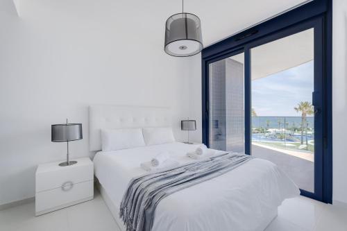 a white bedroom with a bed and a large window at Apartament Sea Senses Summer in Punta Prima