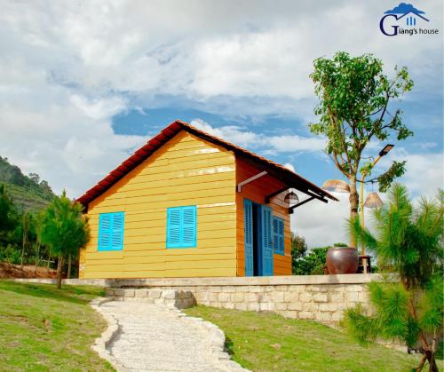ein gelbes und blaues Haus mit einer Steinmauer in der Unterkunft Giăng's House Farmstay & Glamping in Bảo Lộc